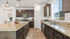 Una cocina moderna con encimeras de granito, armarios de madera oscura, electrodomésticos de acero inoxidable e iluminación colgante.