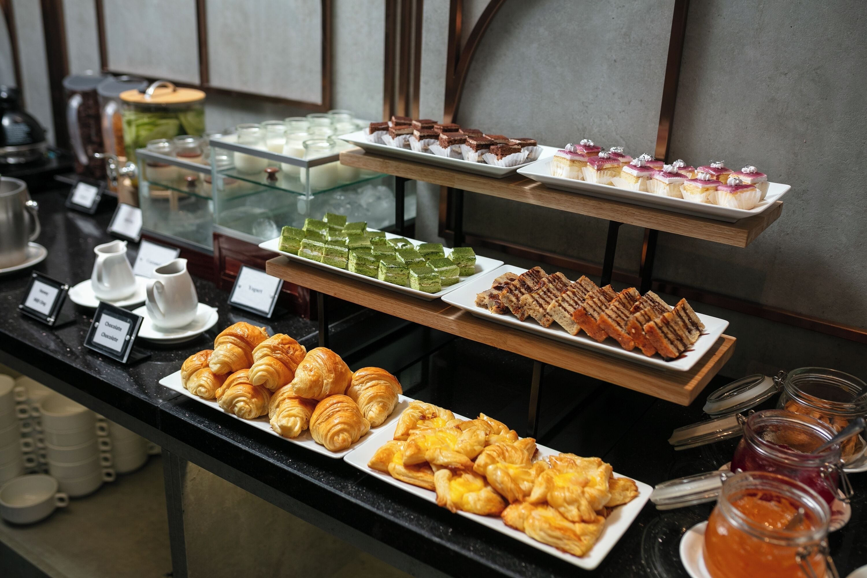 A buffet with various pastries and desserts, including croissants, sandwiches, and cakes.