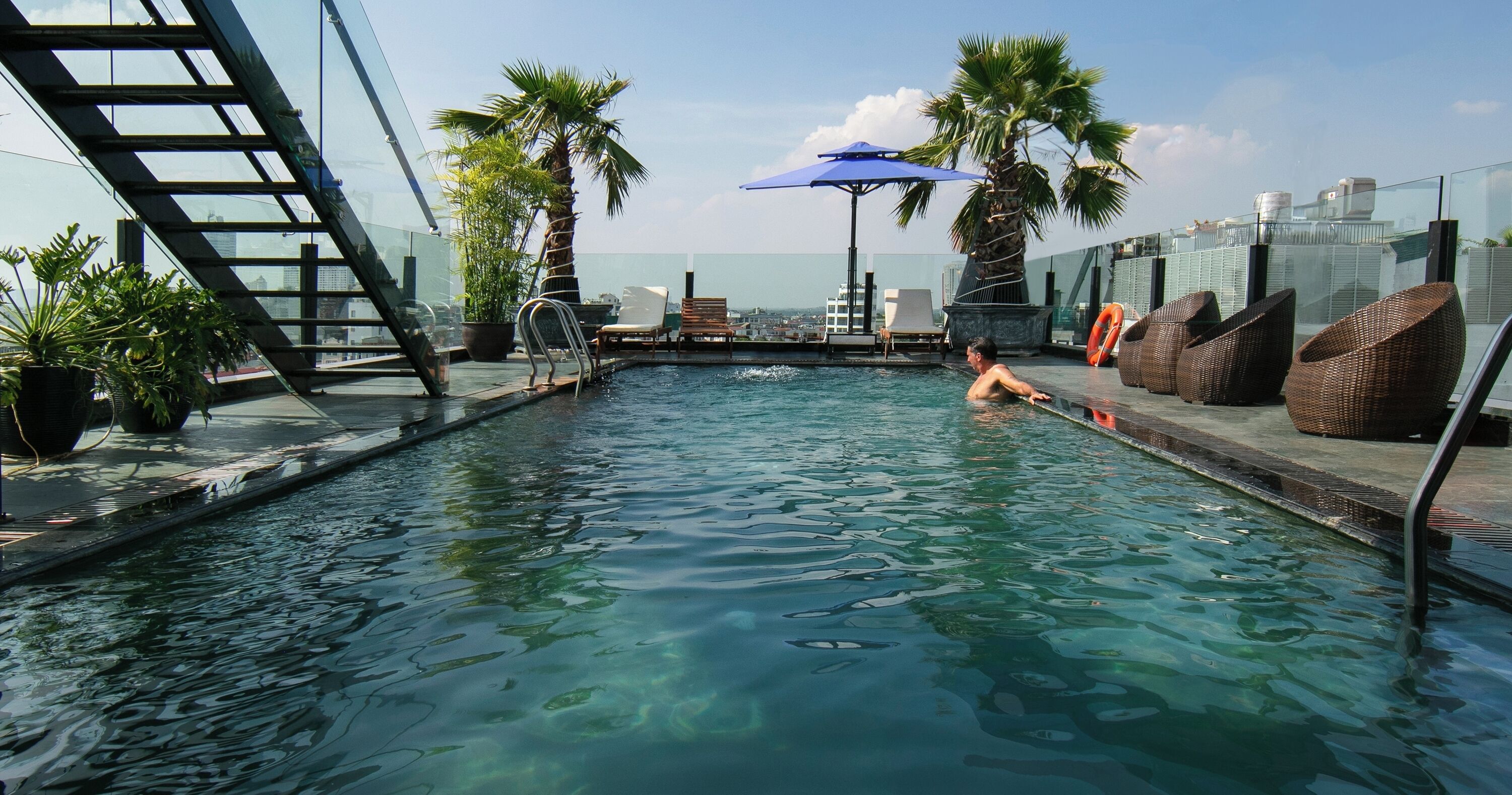 Una piscina en la azotea con agua cristalina, rodeada de sillones de descanso y plantas en macetas.