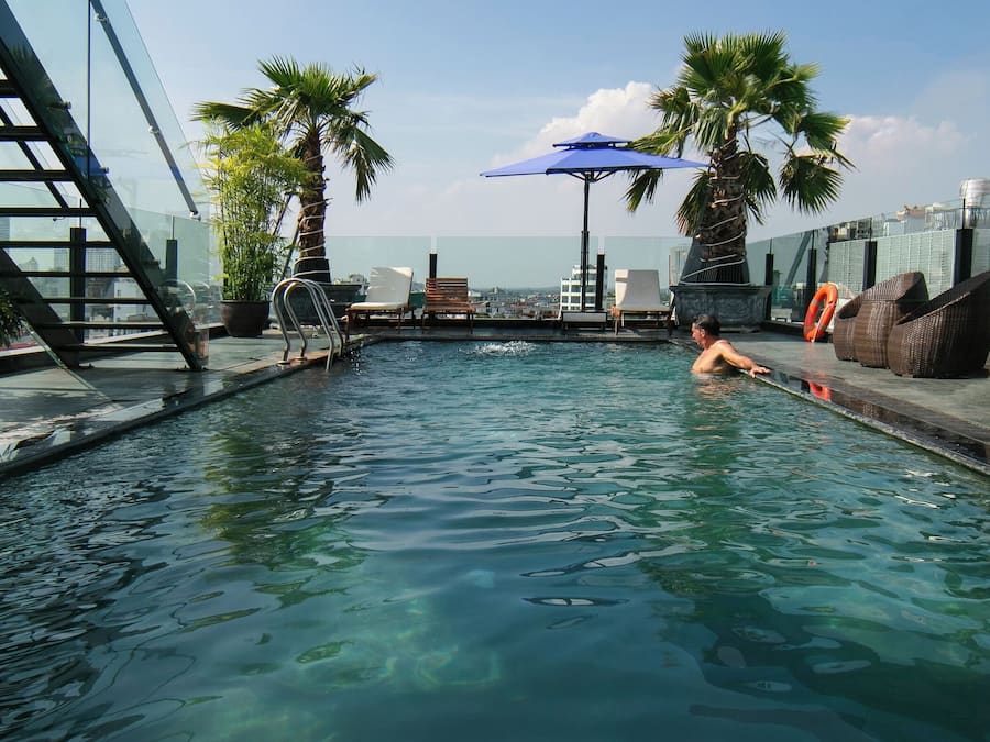 A rooftop pool with clear water, surrounded by lounge chairs and potted plants.