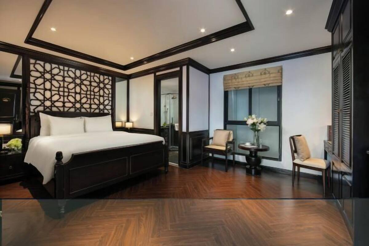 Une chambre dotée d’un grand lit, d’un coin salon avec des fauteuils, d’une petite table et d’un panneau décoratif mural.