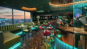 Un área de bar moderna con asientos verdes, una barra y vista a la ciudad.