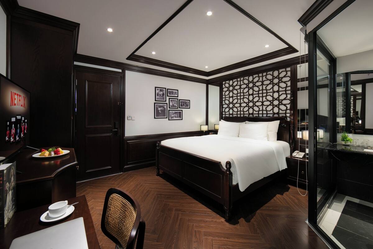 Une chambre d’hôtel avec un grand lit, un bureau avec un ordinateur portable, une chaise, une télévision et un mur orné de tableaux.