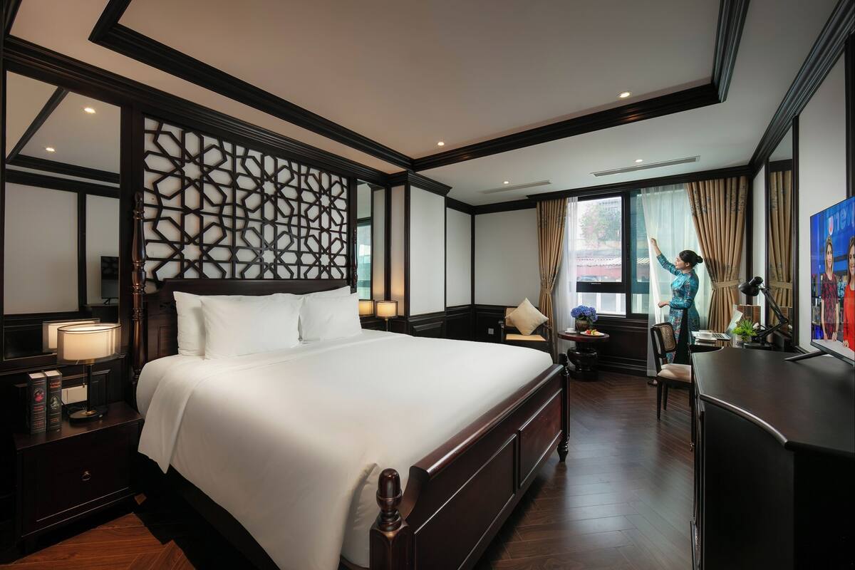 Une chambre d’hôtel avec un grand lit, un bureau, une chaise, une télévision et un panneau décoratif au mur.