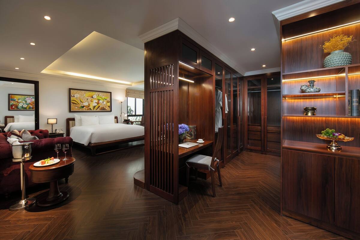 Une chambre d’hôtel comprenant un lit, un bureau avec une chaise, un canapé et une armoire en bois avec des étagères.