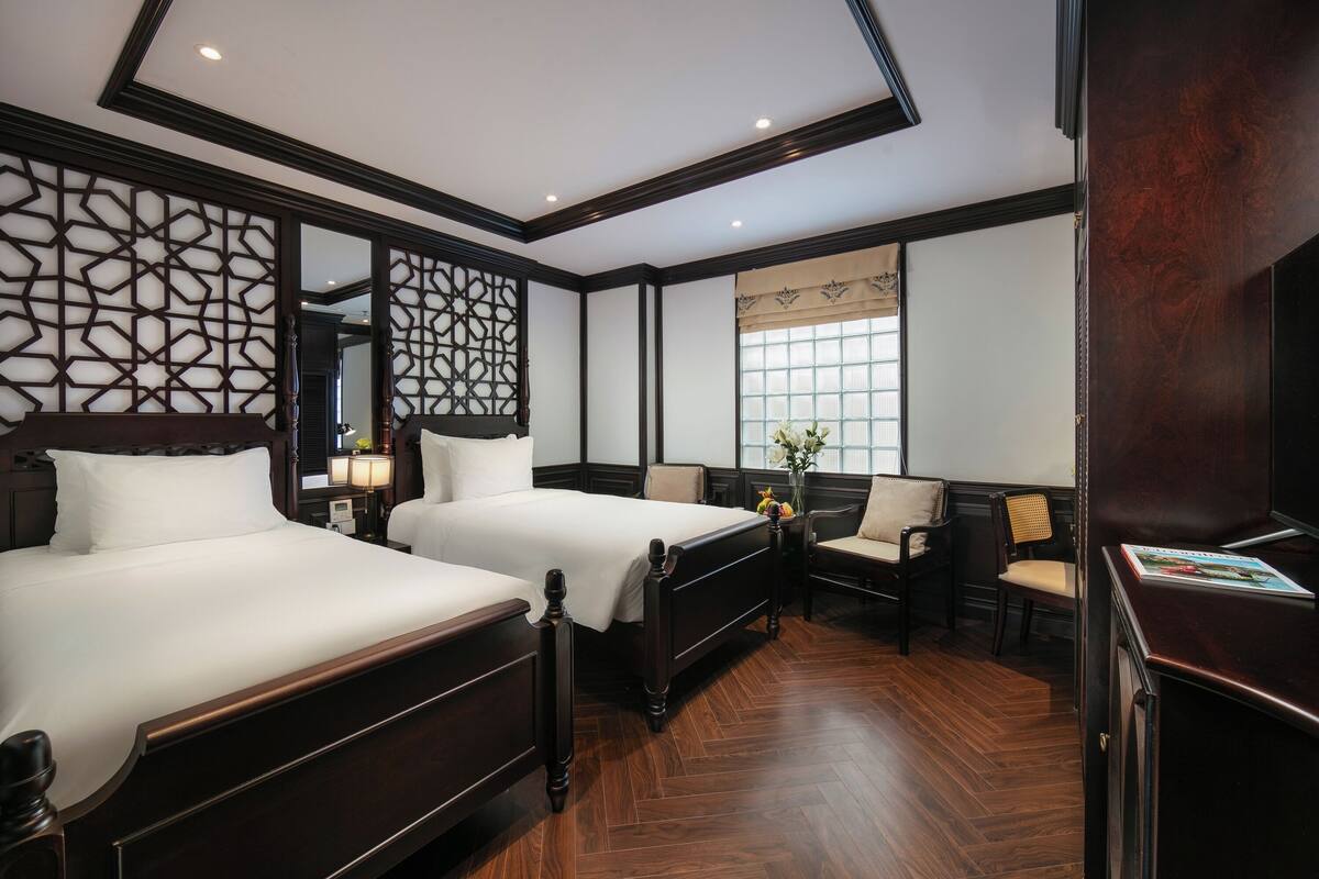 Une chambre d’hôtel avec deux lits, un grand miroir, un panneau décoratif au mur, une fenêtre avec vue et un plancher en bois.