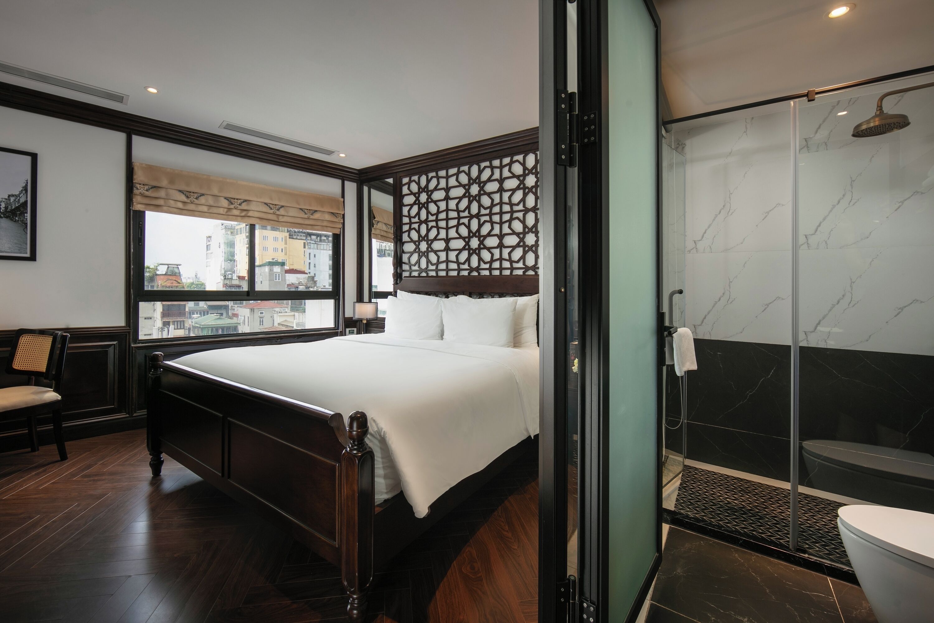 Una habitación de hotel moderna con una cama grande, cabina de ducha de vidrio y vistas a la ciudad a través de una ventana.