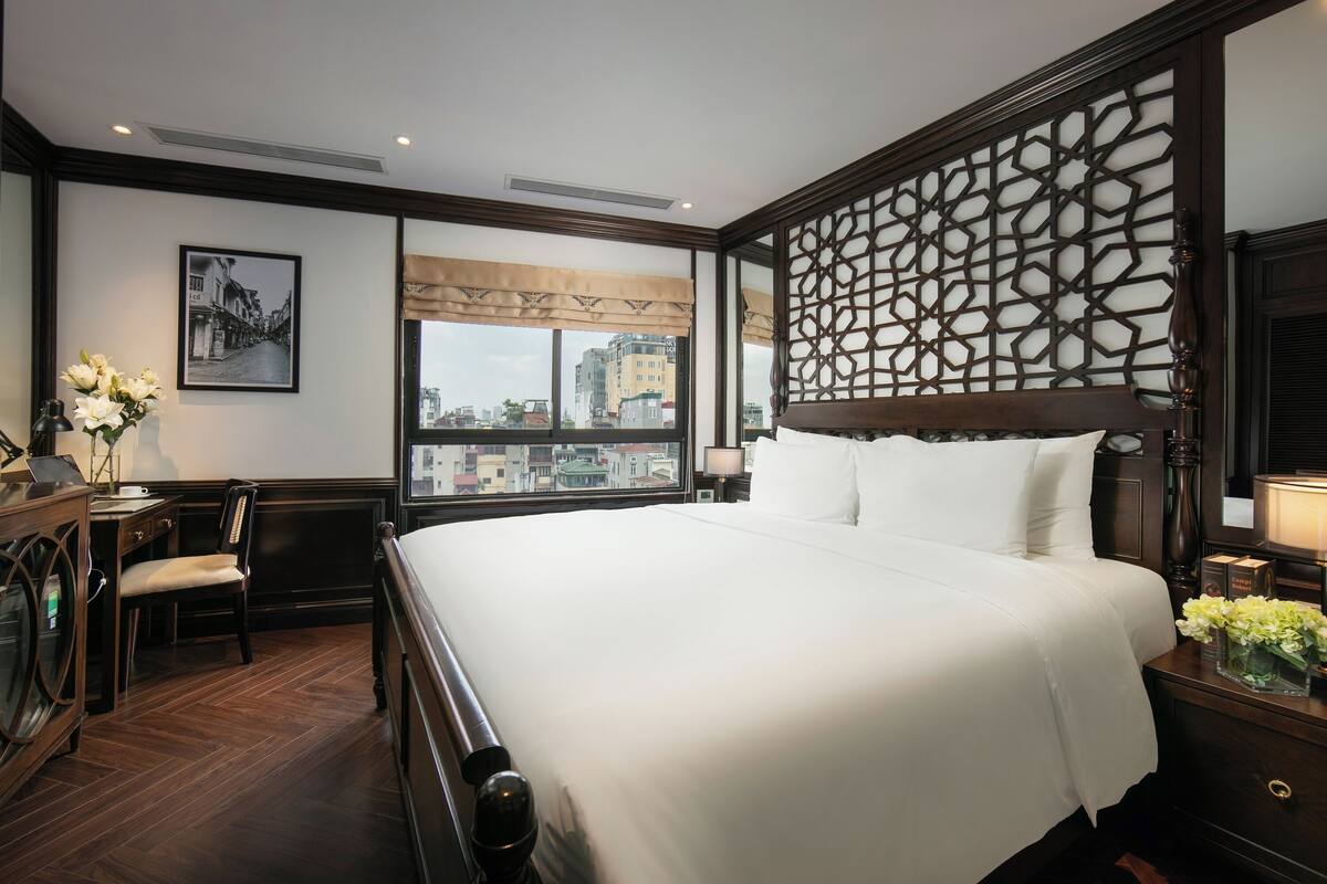 Une chambre d’hôtel avec un grand lit, un bureau avec une chaise, une fenêtre donnant sur la ville et un panneau décoratif au mur.