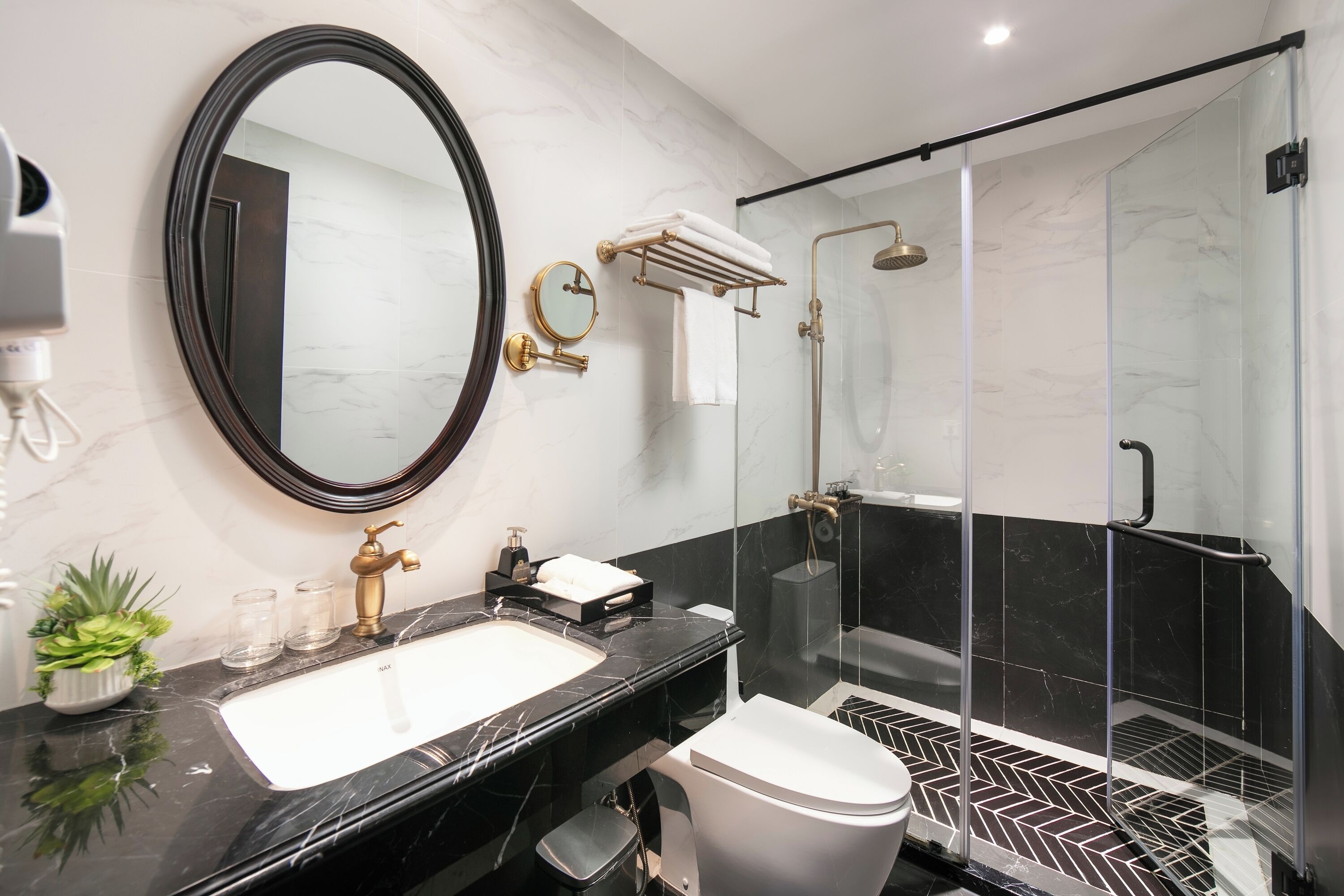 Un baño moderno con lavamanos de mármol negro, un espejo grande, un grifo dorado, un inodoro blanco y una zona de ducha con mampara de cristal.