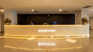 A reception desk with two staff members, a wooden reception desk, and a polished stone floor. - Zecon Hotel (Kuala Lumpur)