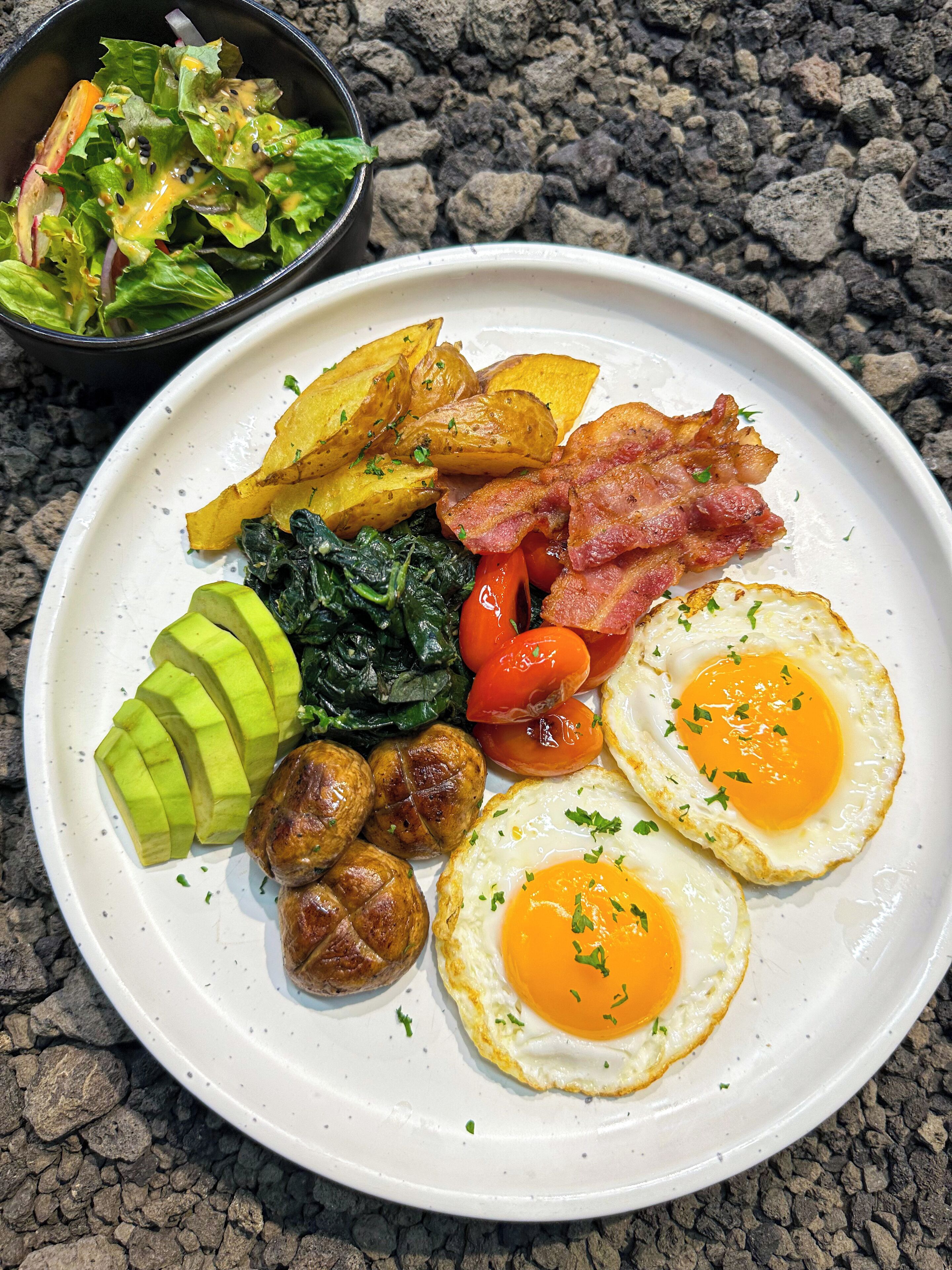 A breakfast plate with eggs, bacon, potatoes, tomatoes, and greens.