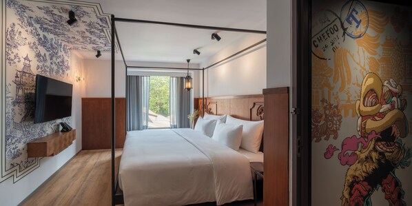 A hotel room with a bed, a TV, a wooden nightstand, and a wall with a traditional mural.