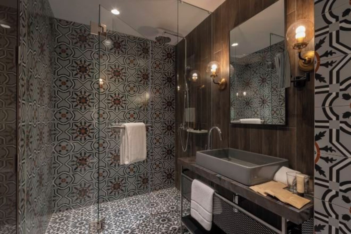A modern bathroom with patterned tiles, a glass shower enclosure, a large mirror, and a built-in sink.