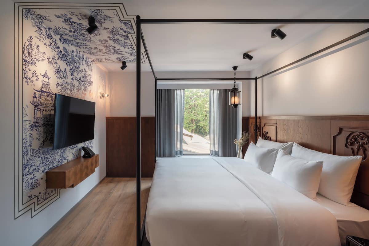 A modern hotel room with a large bed, a mounted TV, and a view of the outdoors.