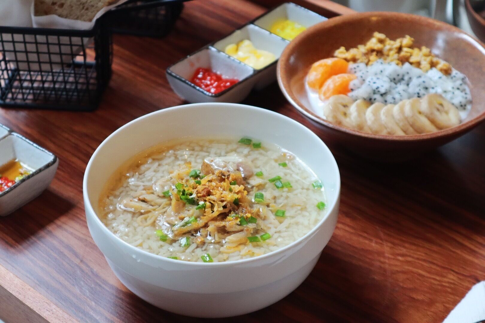 A bowl of rice with toppings, accompanied by small bowls of condiments and a bowl of fruit.