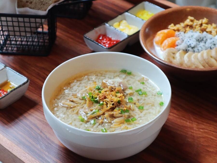 A bowl of rice with toppings, accompanied by small bowls of condiments and a bowl of fruit.