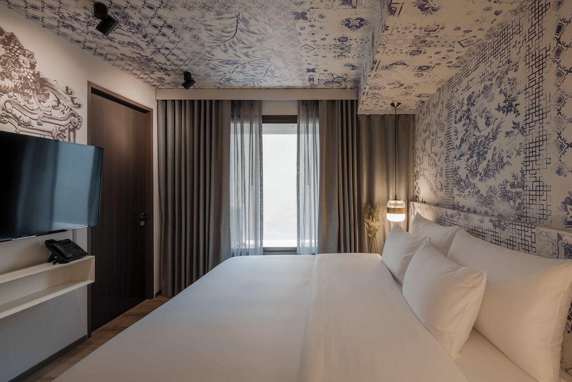 A hotel room with a large bed, a flat-screen TV, a telephone, and a window with curtains.