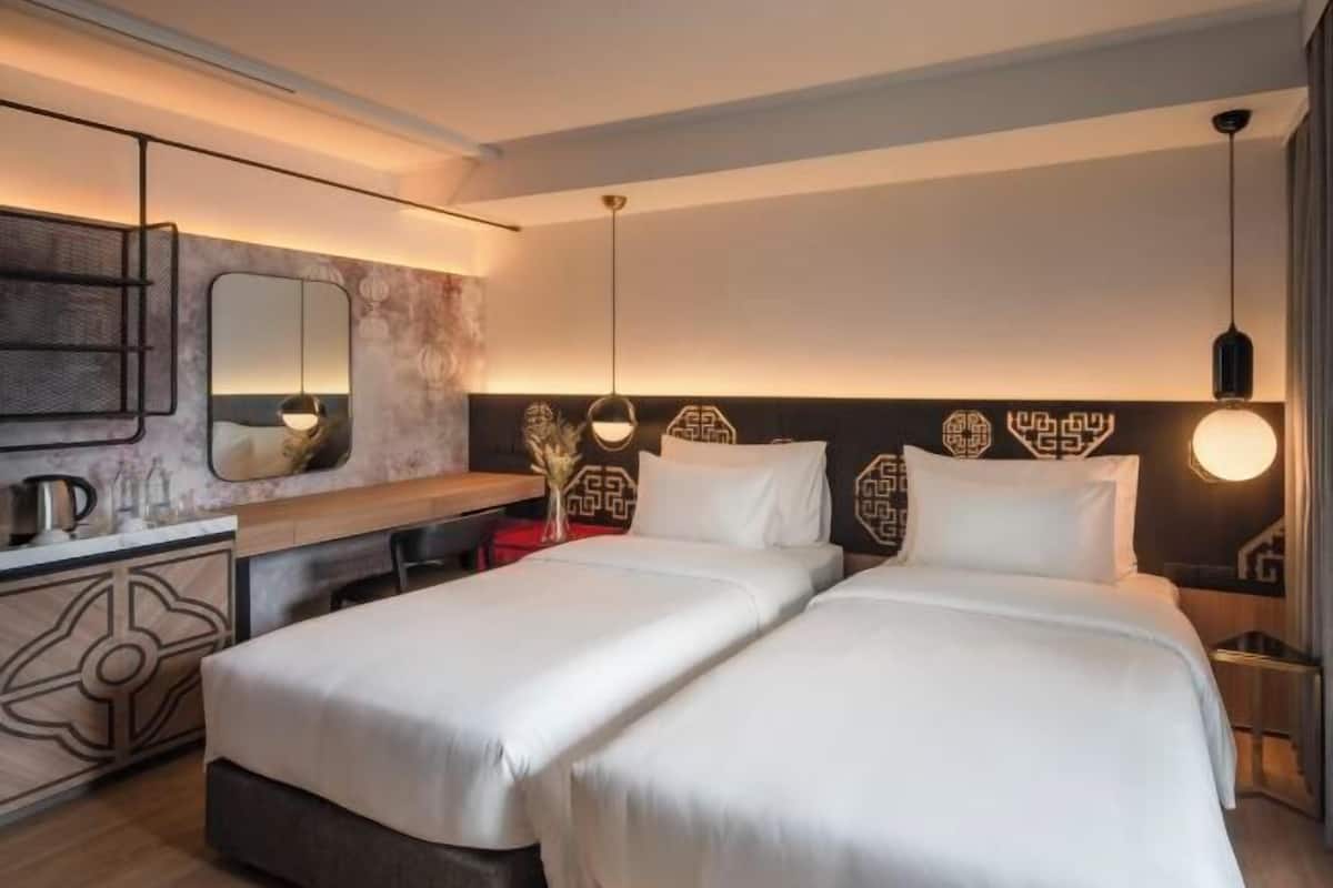 A hotel room with two beds, a desk, a mirror, and a decorative wall.