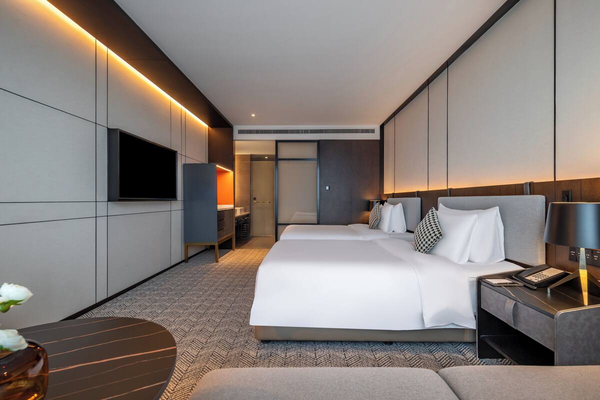 A modern hotel room with a large bed, bedside tables, a flat-screen TV, and a desk with a lamp.