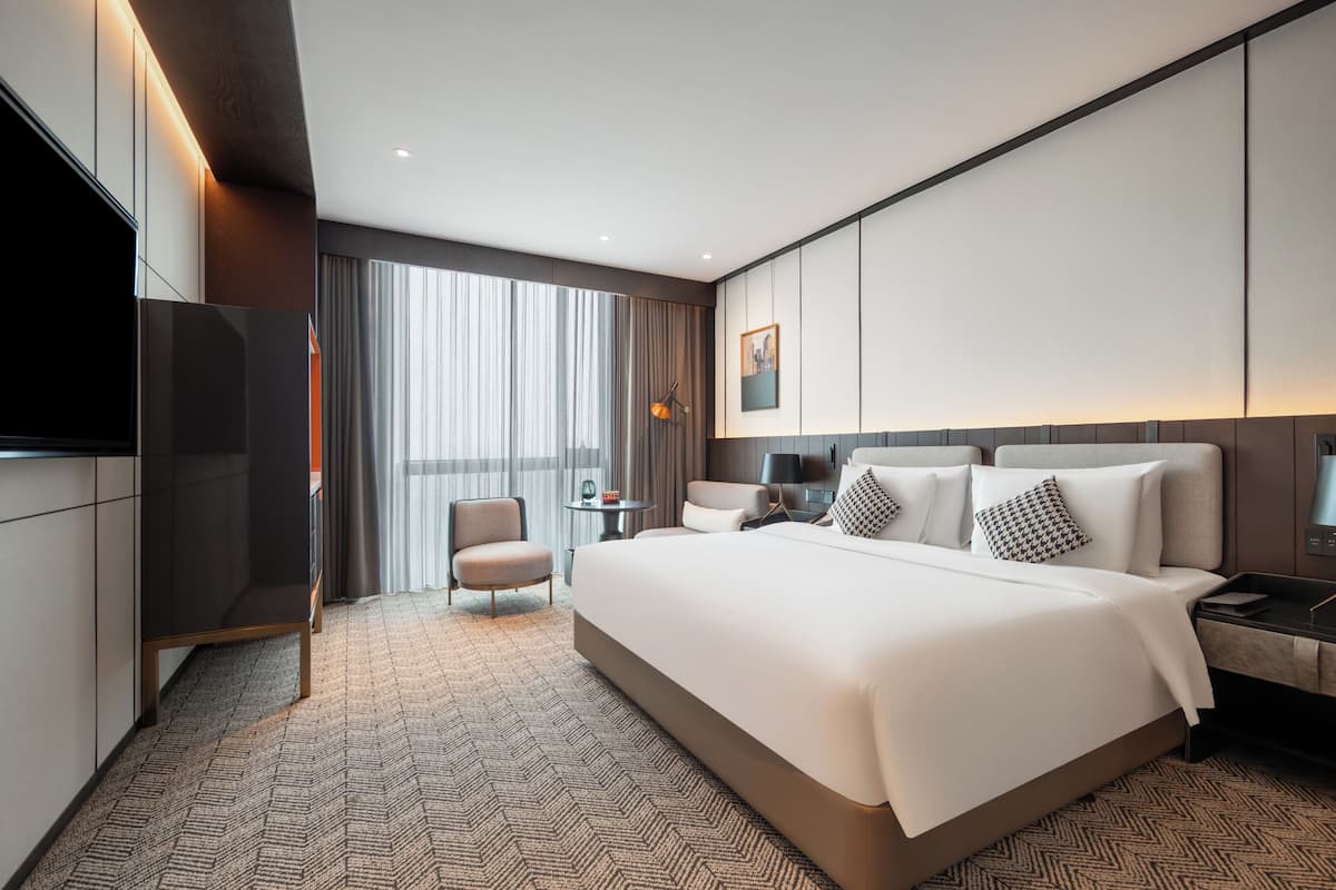A modern hotel room with a large bed, a TV, a desk, and a chair.