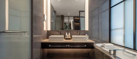 A modern bathroom with a large mirror, two sinks, a shower area, and a view of the city through large windows.