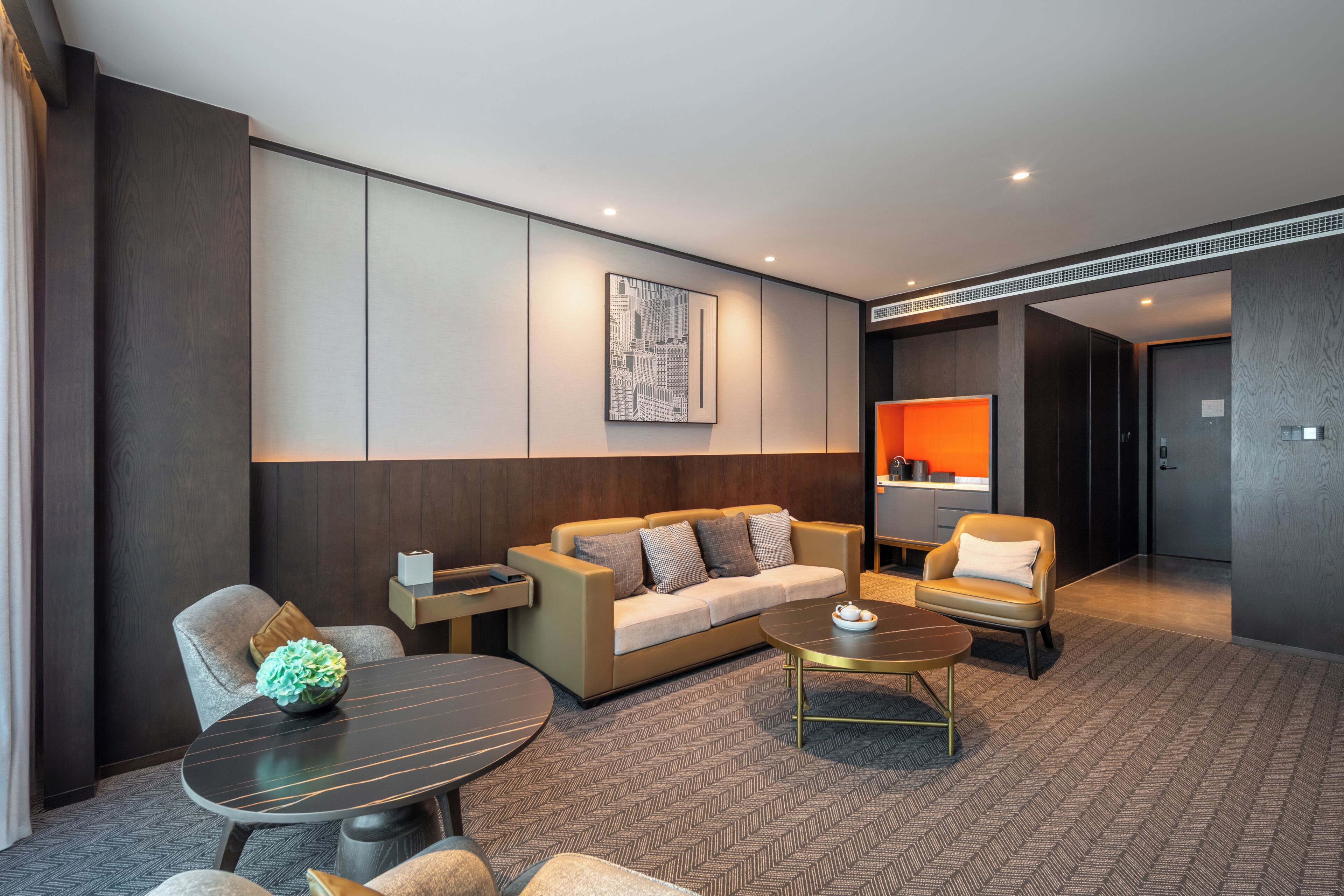 Quarto de hotel moderno com sofá, poltronas, mesa de centro e mesa de jantar.