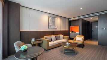 Quarto de hotel moderno com sofá, poltronas, mesa de centro e mesa de jantar.