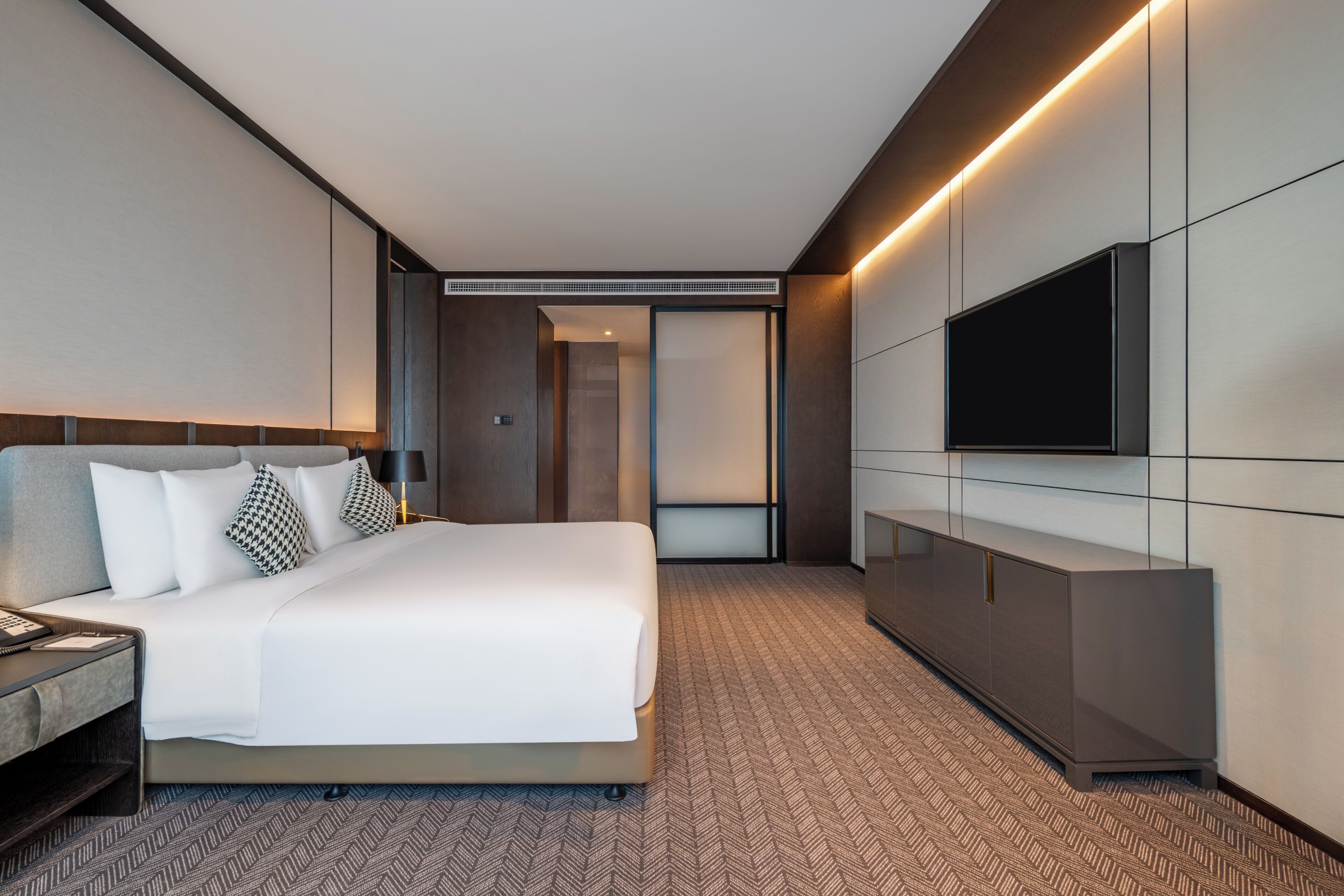 A modern hotel room with a large bed, a flat-screen TV, a minibar, and a walk-in closet.