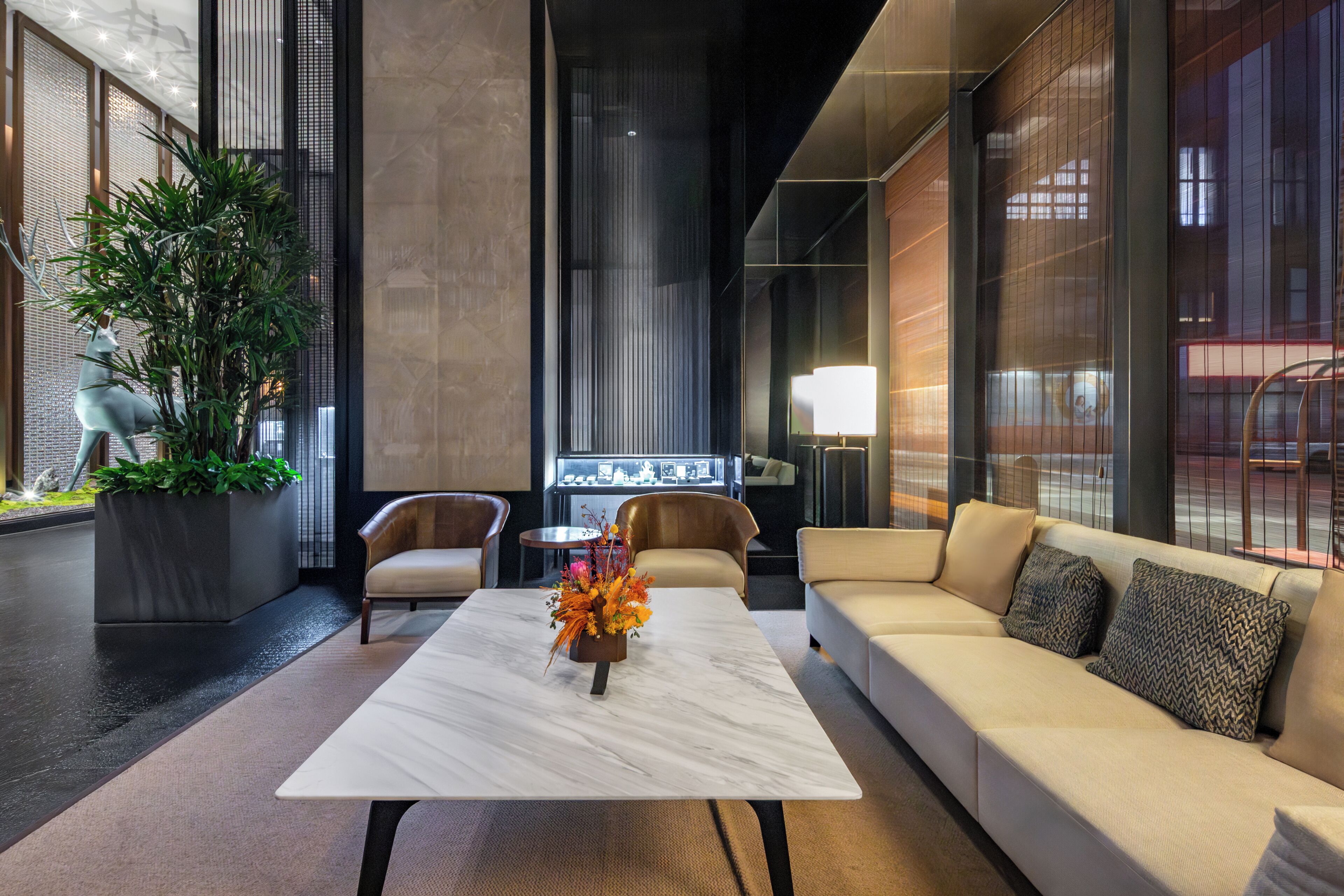 A modern lobby with a marble coffee table, leather sofas, a potted plant, and a display case.