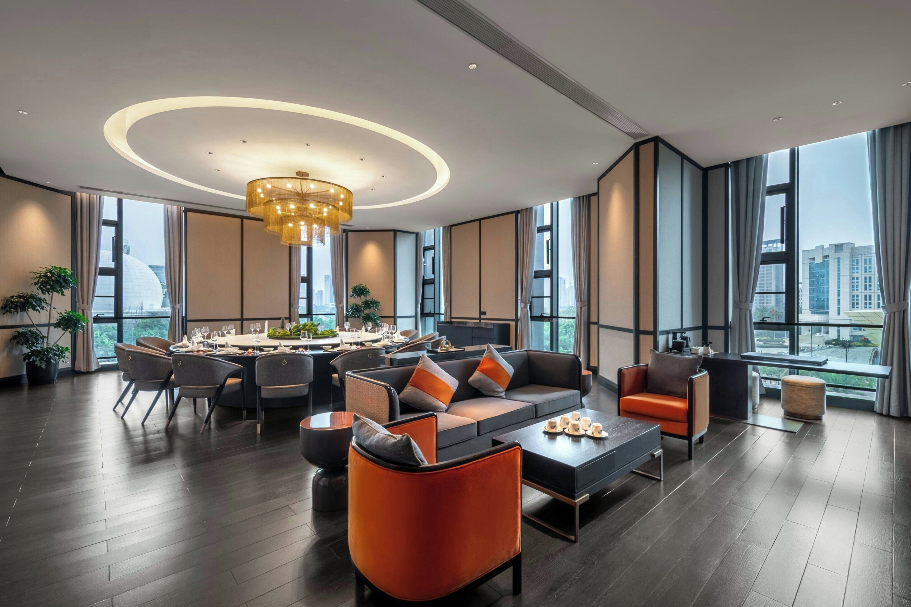 A spacious living area with a modern sofa, dining table, and chairs, large windows with city views, and a chandelier.