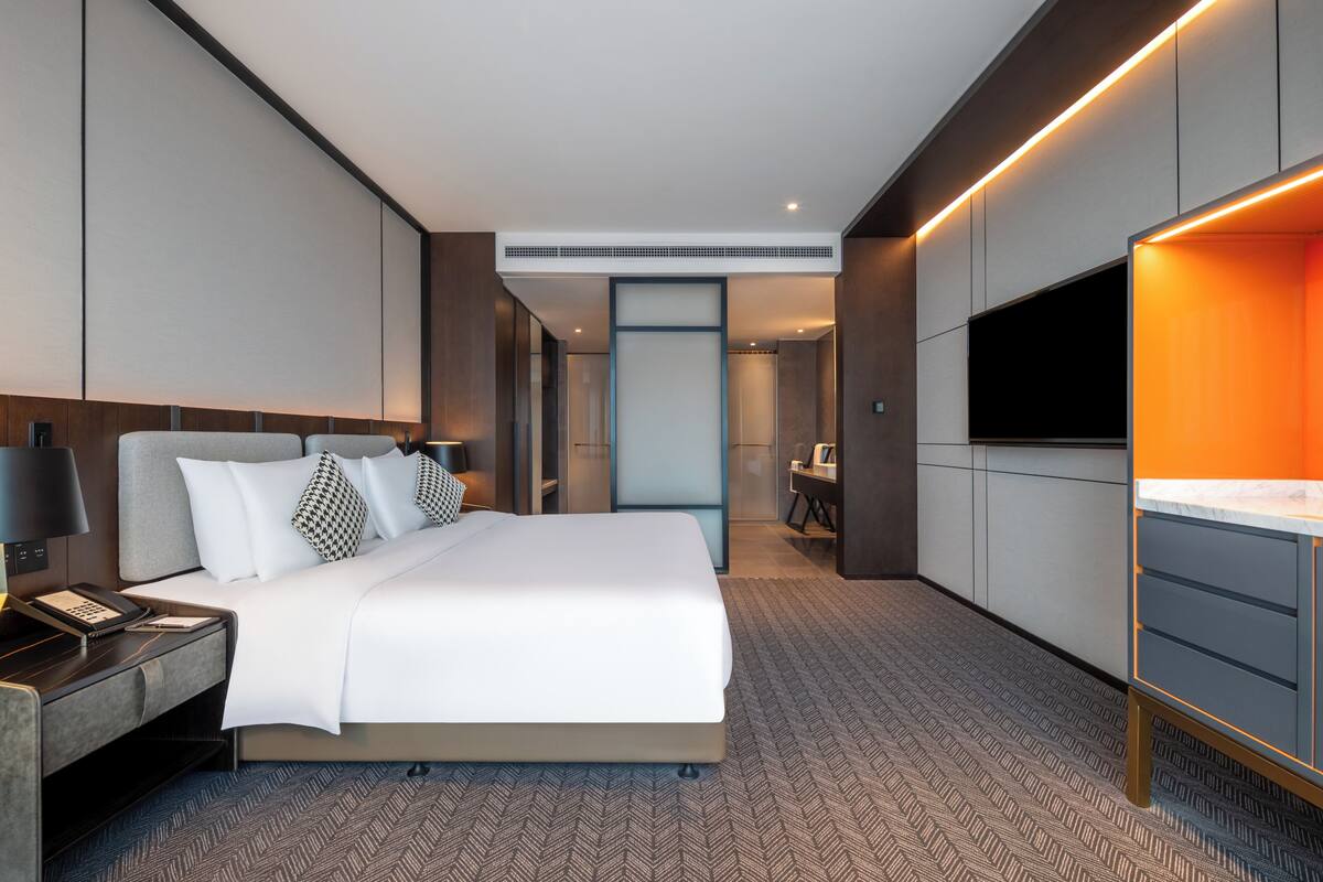 A modern hotel room with a large bed, a desk, a flat-screen TV, and a built-in air conditioning unit.