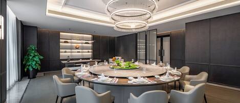 A modern conference room with a round table, chairs, a chandelier, and a plant.