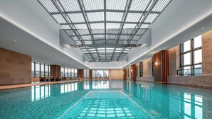 Une grande piscine intérieure dotée d’un toit en verre, de murs recouverts de panneaux de bois et de grandes fenêtres.