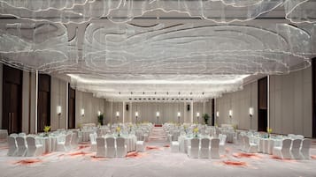 Un amplio salón de conferencias con mesas redondas, sillas blancas y suelo de mármol.