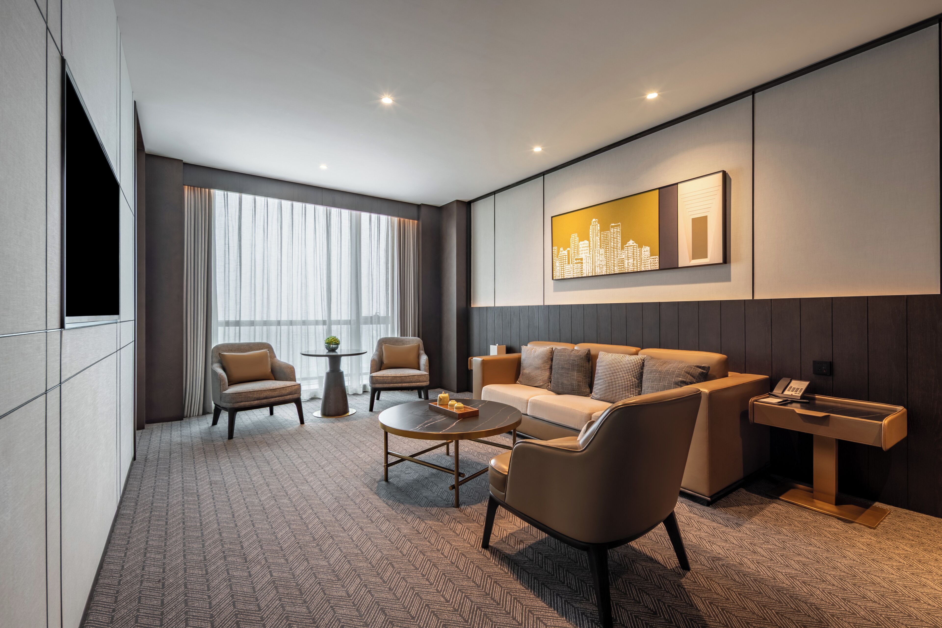 A modern hotel room with a sofa, armchairs, a coffee table, a side table, and a cityscape artwork on the wall.