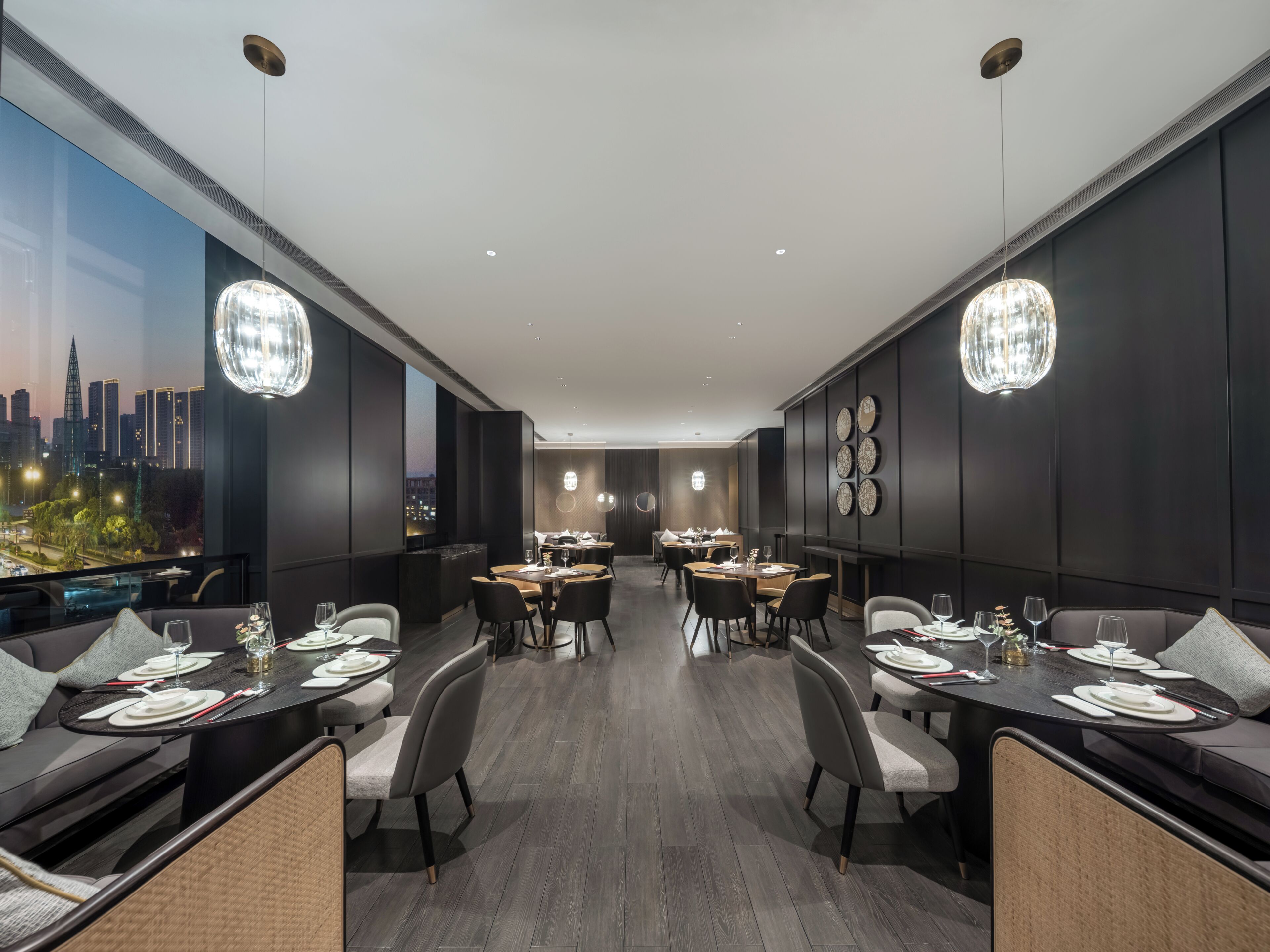 A modern dining area with multiple tables and chairs, a city view through large windows, and decorative wall art.