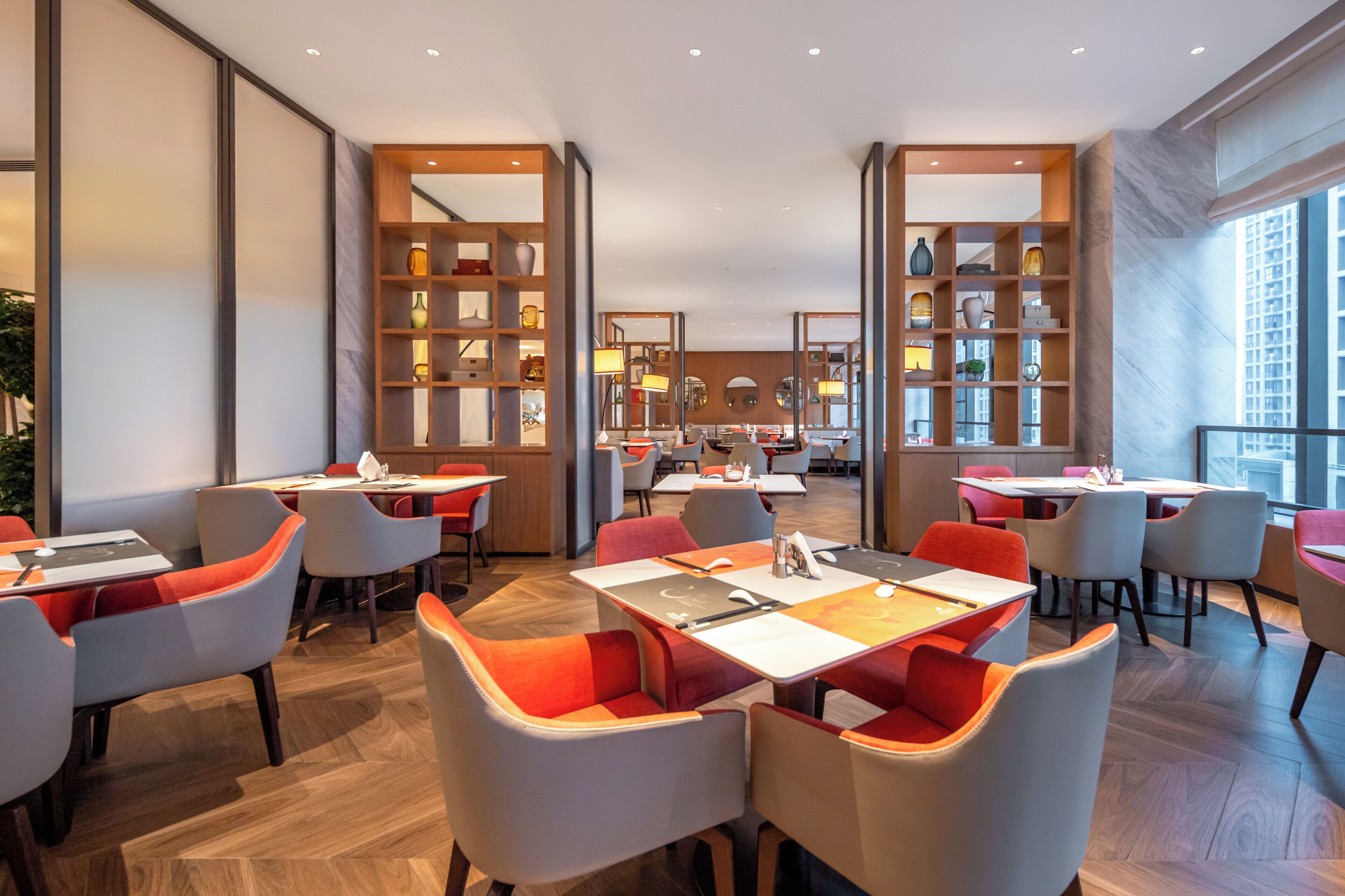 Un restaurante moderno con mesas y sillas altas, una zona de estar central y amplios ventanales.