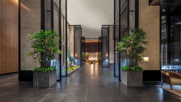 Un hall d’hôtel moderne avec un comptoir d’accueil central, des plantes en pot et un espace salon.