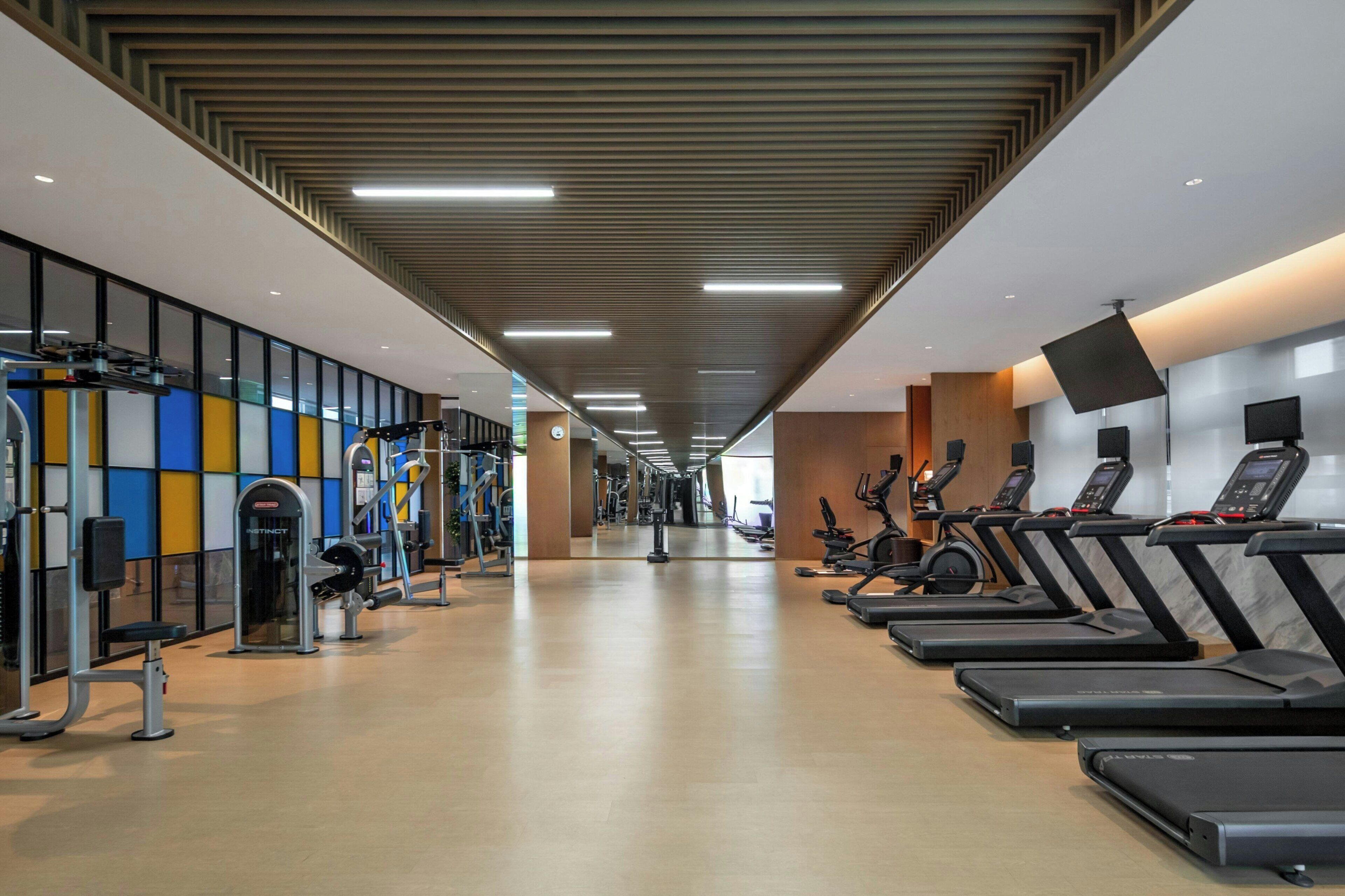 Une salle de sport équipée de tapis de course, d’appareils de musculation et d’un mur recouvert de miroirs.