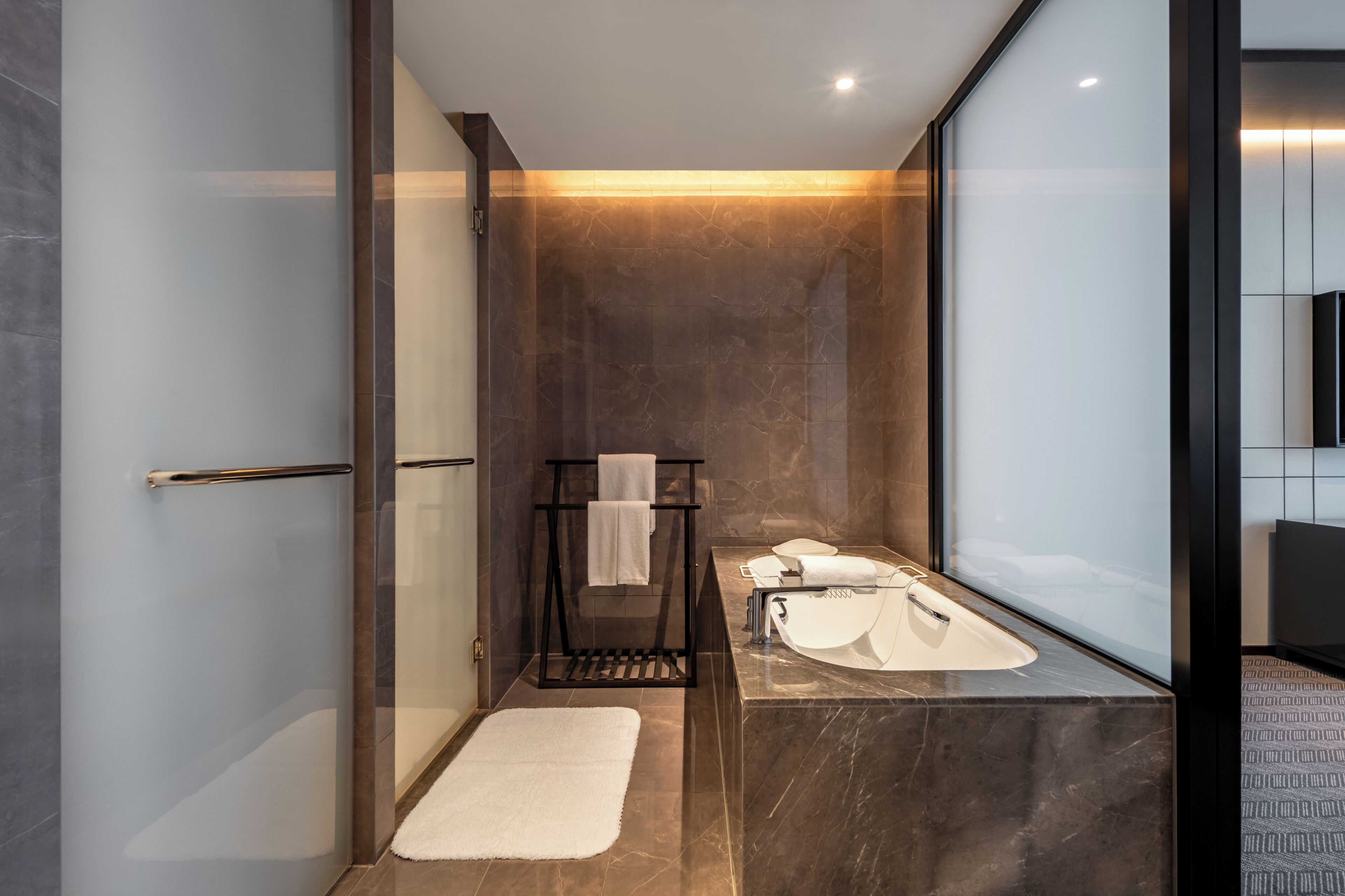 A modern bathroom with a glass shower enclosure, a black towel rack, a white sink, and a large mirror.