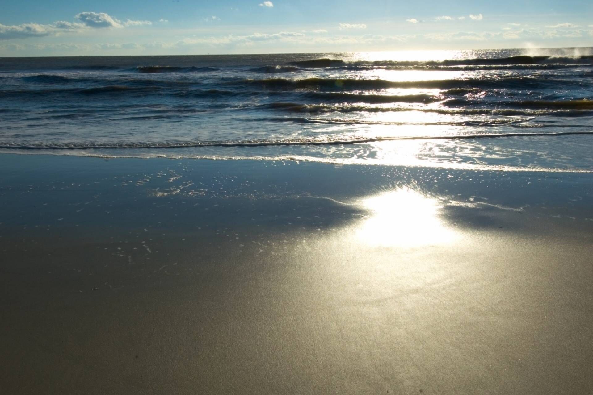 En strand där solljuset reflekteras i den våta sanden.