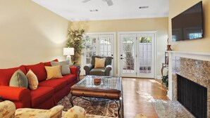 A living room with a red sofa, a glass coffee table, a fireplace, and a ceiling fan. - Guest Favorite Beckenham Townhouse, Walk to Beach, Pool, Private Courtyard, Port Royal Village (Hilton Head Island)
