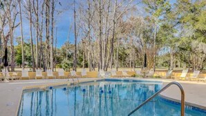 A swimming pool with a metal ladder, surrounded by lounge chairs and trees. - Guest Favorite Beckenham Townhouse, Walk to Beach, Pool, Private Courtyard, Port Royal Village (Hilton Head Island)