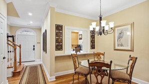 A dining area with a chandelier, wooden chairs, a white door, and a hallway with a wooden staircase. - Guest Favorite Beckenham Townhouse, Walk to Beach, Pool, Private Courtyard, Port Royal Village (Hilton Head Island)