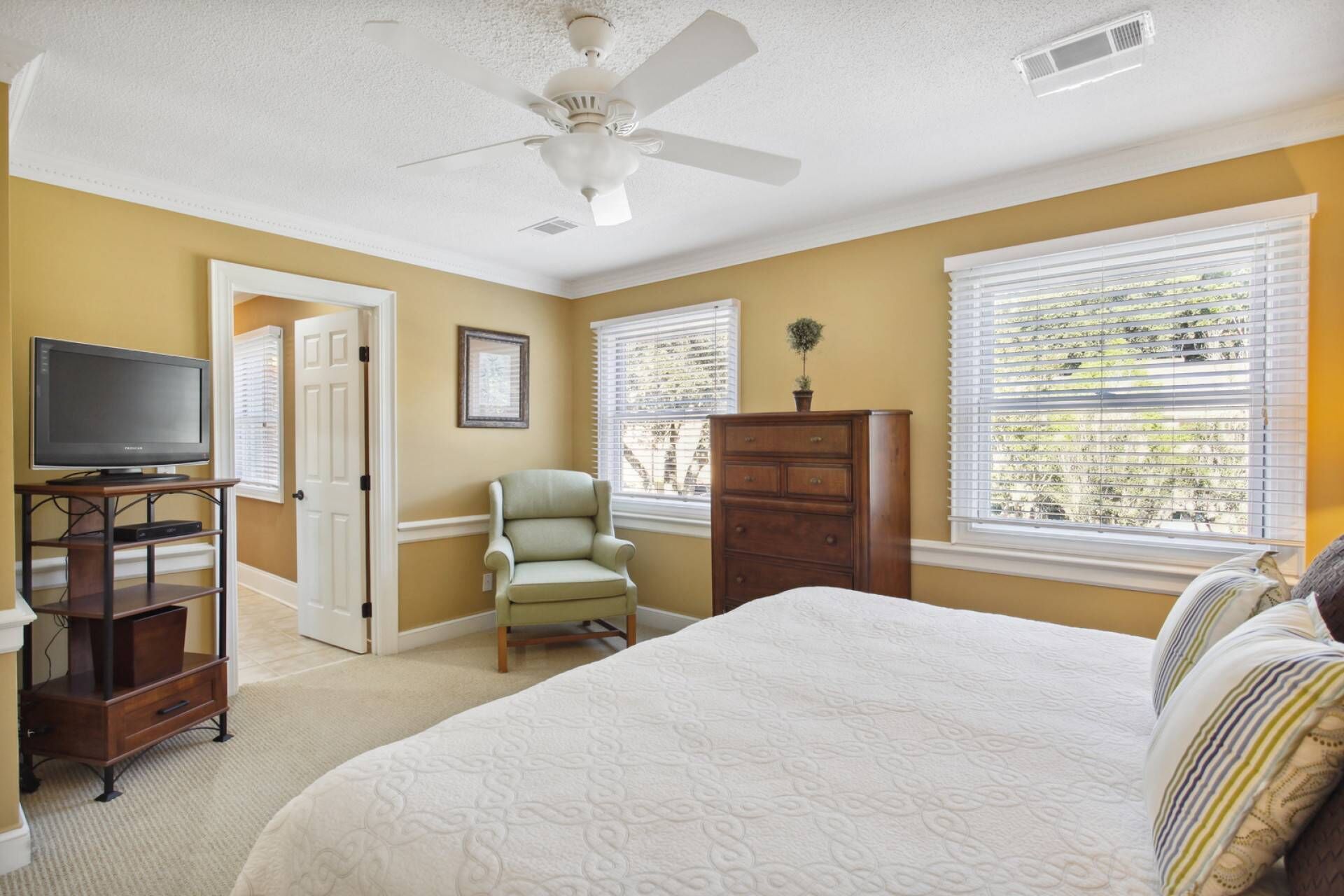 A bedroom with a bed, a TV on a stand, a chair, a dresser, and a ceiling fan.
