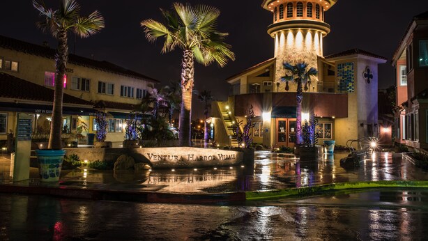 Una plaza bien iluminada con una fuente, palmeras y un edificio con una torre.
