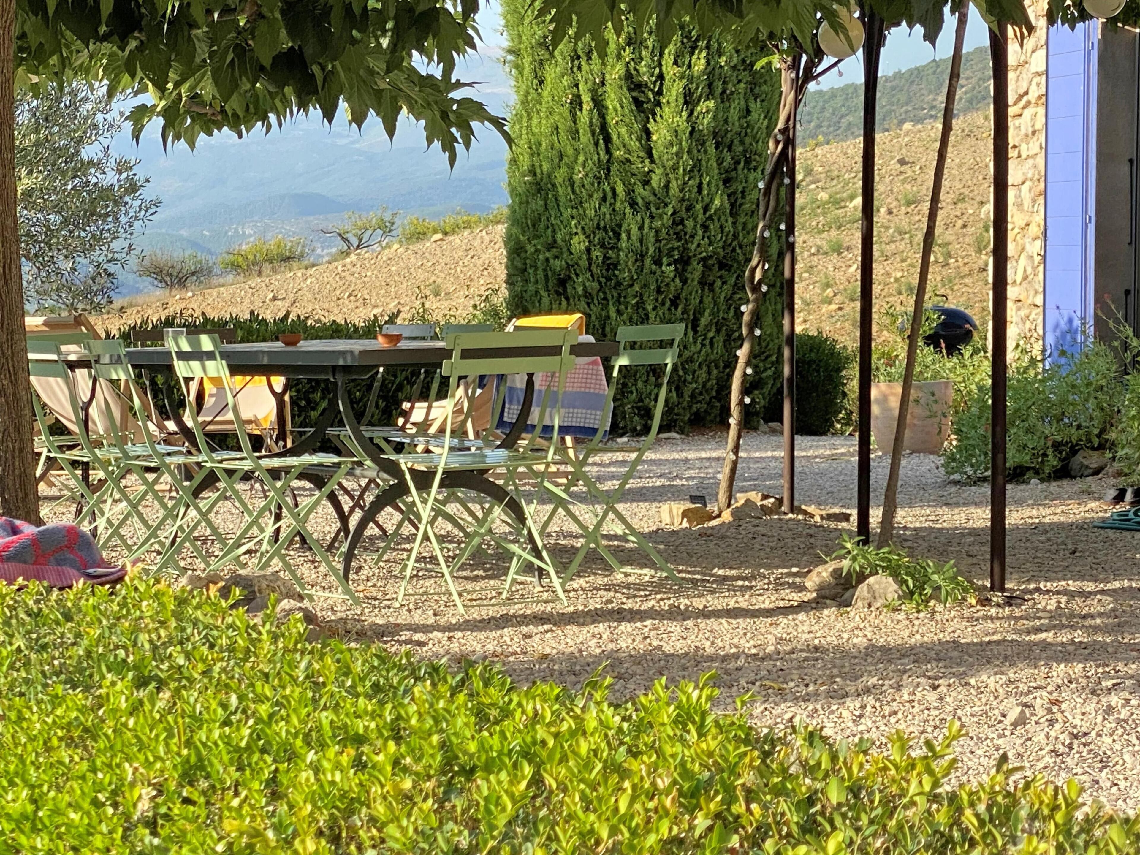 An outdoor seating area with a table and chairs, surrounded by greenery and a view of the landscape.