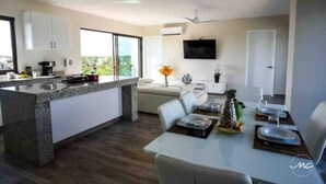 A modern kitchen with a large island, a dining area with a table set for two, and a flat-screen TV mounted on the wall. - Blue Luxury La Veleta (Tulum)