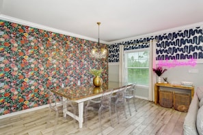 Un comedor con papel tapiz floral, una mesa con cubierta de vidrio y sillas transparentes.