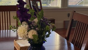 Una mesa de comedor con un centro de mesa floral, salerosos y pimenteros, y una cesta tejida.